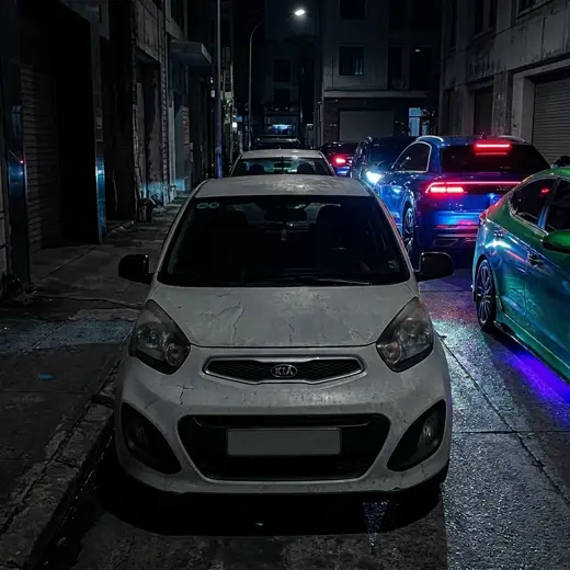 Carro blanco perdido entre carros con luces de neón en la calle